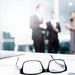 Glasses on desk with blurred business meeting