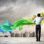 Businessman painting colorful paint swirl over city skyline