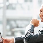 Smiling businessman holding tablet in bright office